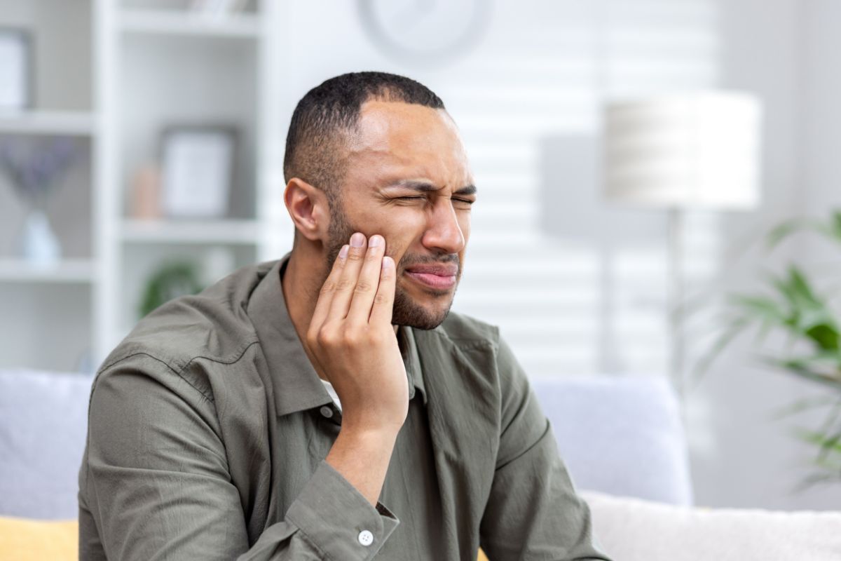 Man holding his cheek experiencing tooth pain in a dental office setting.