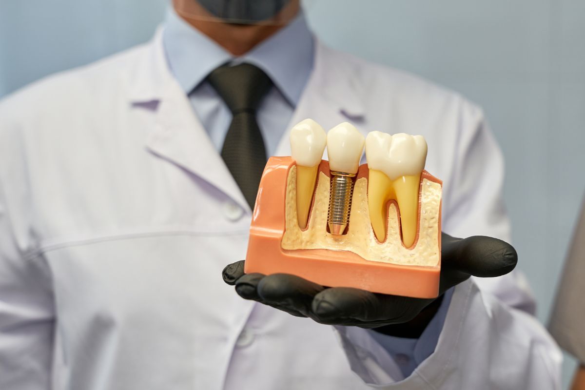 Dentist holding dental implant model showing tooth replacement procedure in Queen Creek.