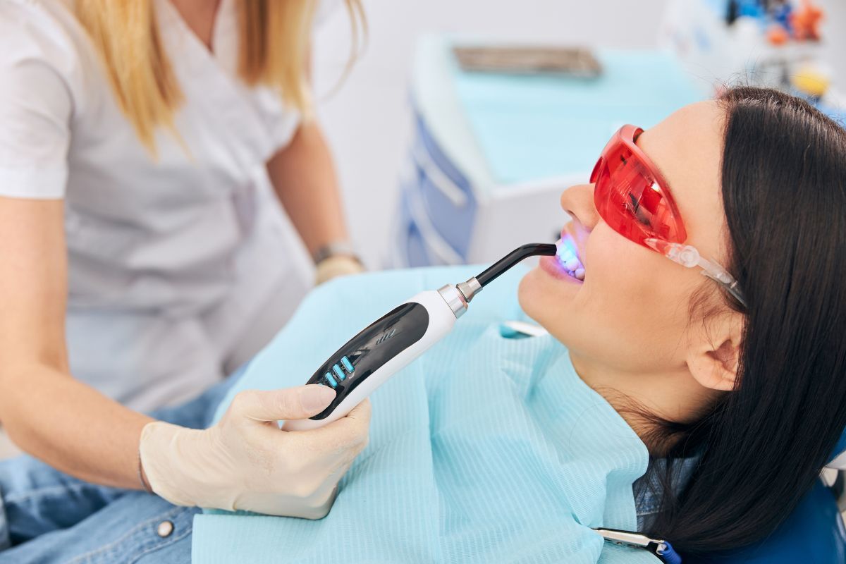 Dentist applying professional whitening treatment to patient's teeth using UV light technology.