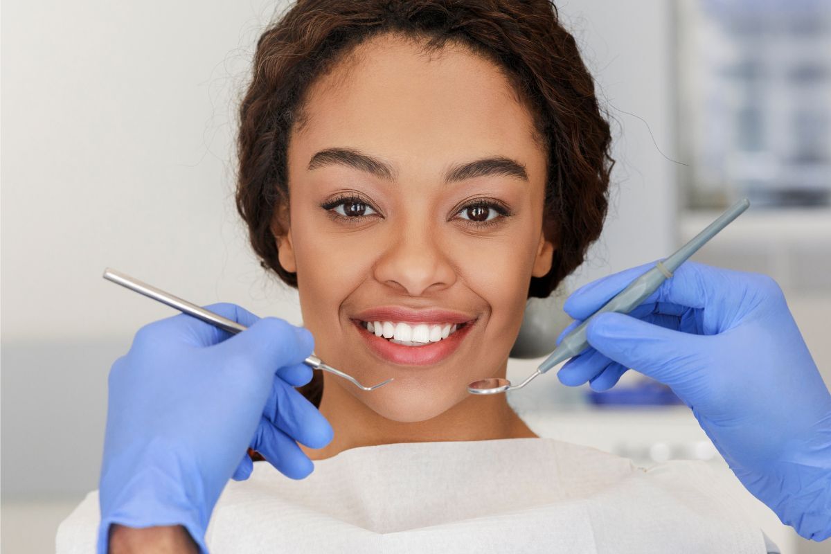 Patient smiling while dentist examines teeth with dental instruments during cosmetic dentistry consultation.