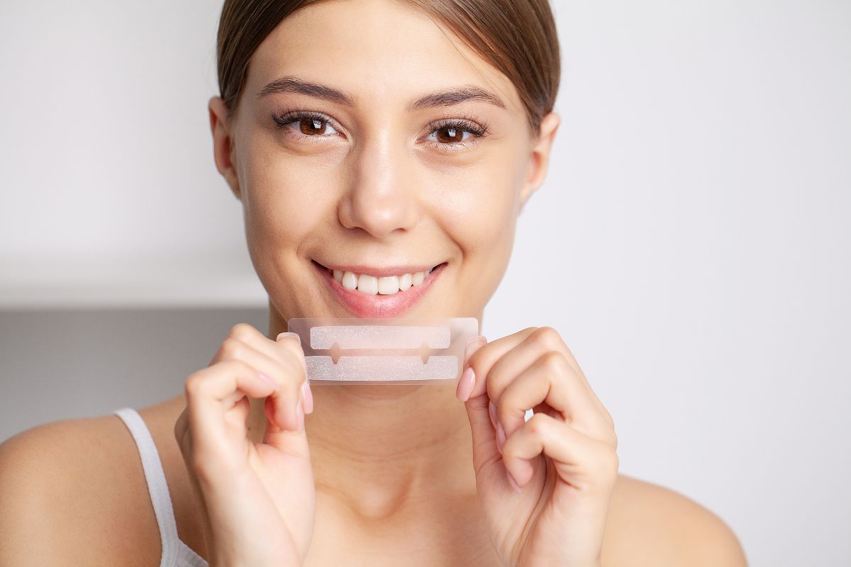Woman holding teeth whitening strips while showing her teeth.