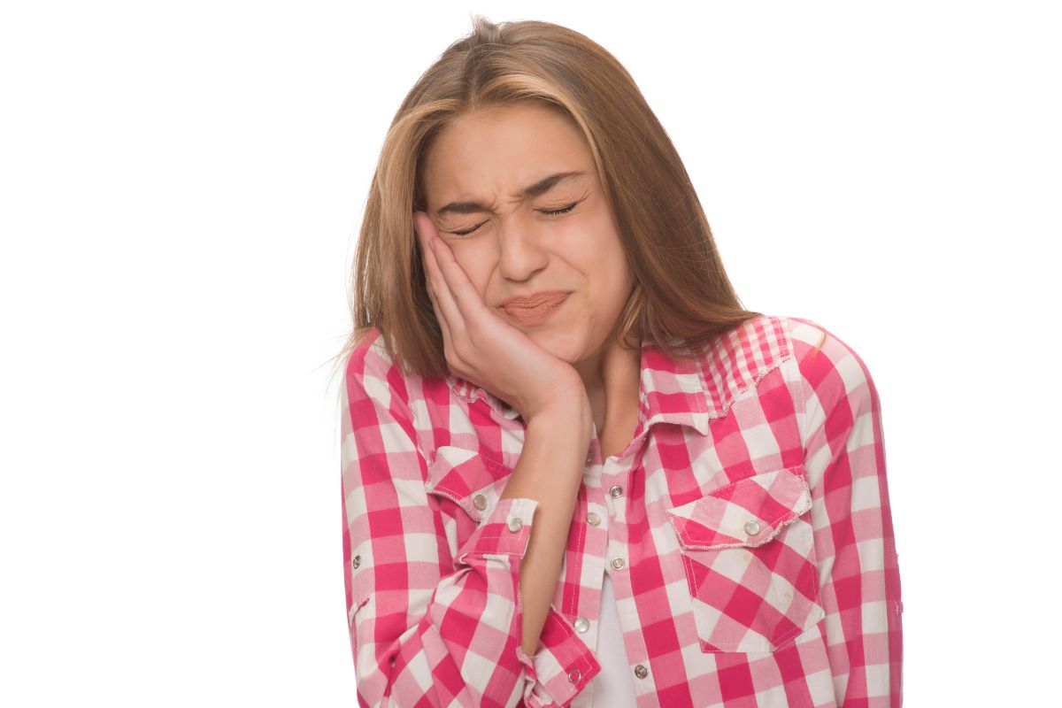 Teenage girl holding her cheek with her eyes closed while experiencing toothache pain.